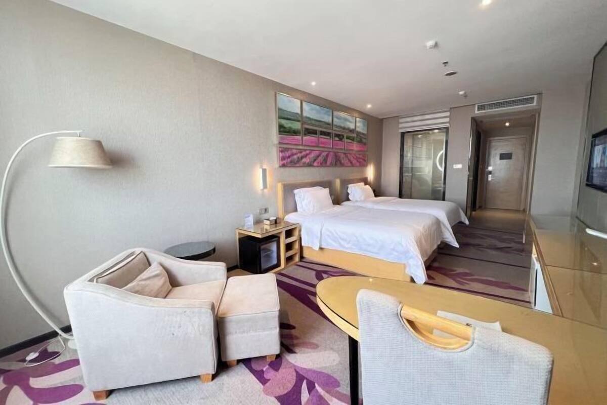 Habitación de hotel con dos camas, un sofá, una mesita, una lámpara y un cuadro en la pared.