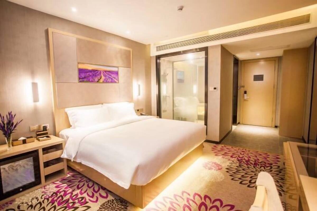Habitación de hotel moderna con una cama grande, un escritorio y zona de ducha con paredes de vidrio.