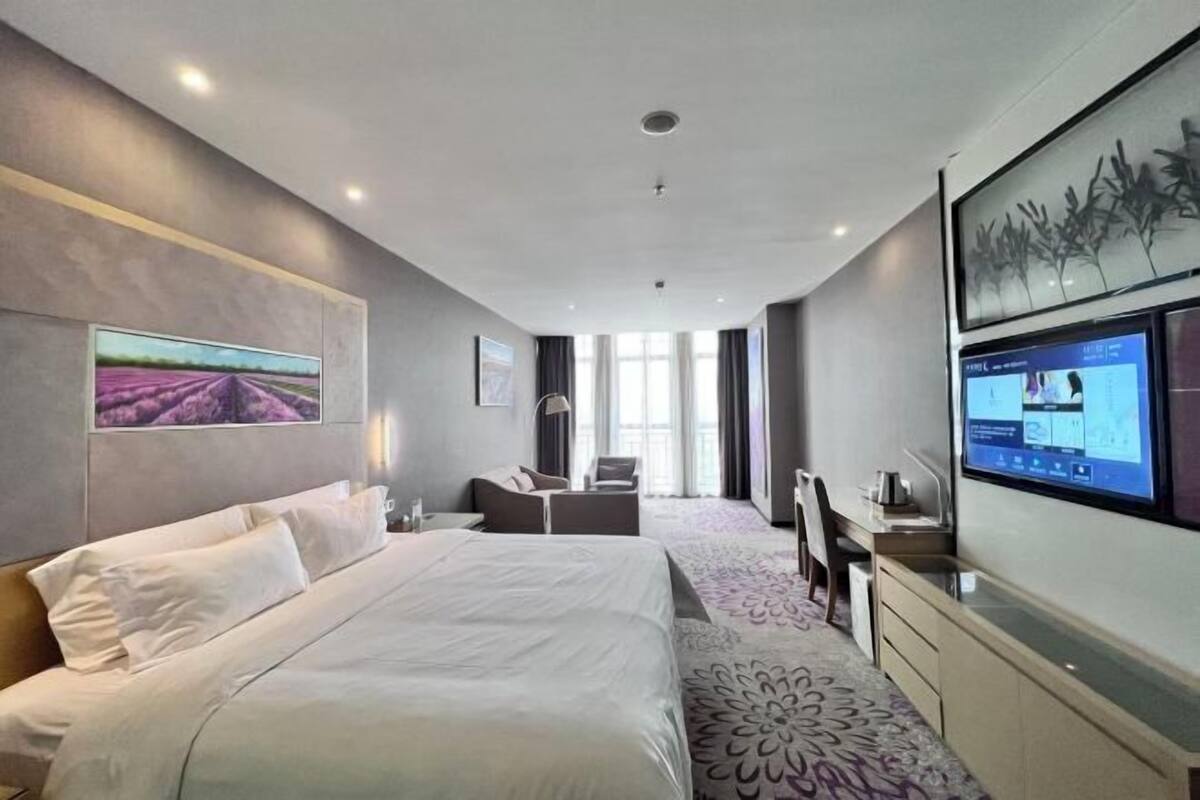 Habitación de hotel moderna con una cama grande, un escritorio, una silla, un televisor y una ventana con cortinas.