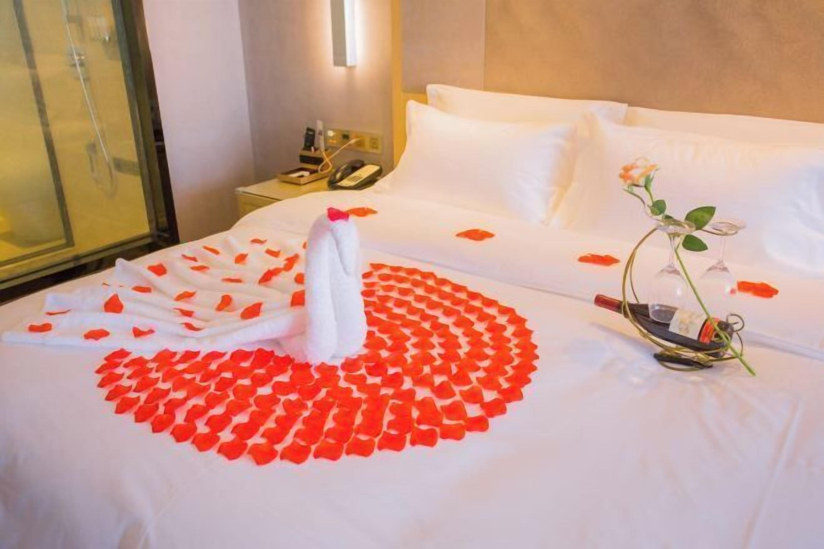 A hotel room with a neatly made bed, a vase with a single flower, and a telephone on the nightstand.