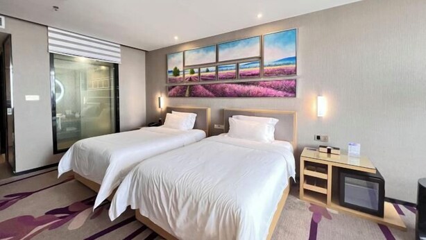 A hotel room with two beds, a glass door leading to a bathroom, a painting of a landscape, and a small TV on a wooden stand. - Lavande Hotel (Huizhou Yuanzhou) (Boluo)