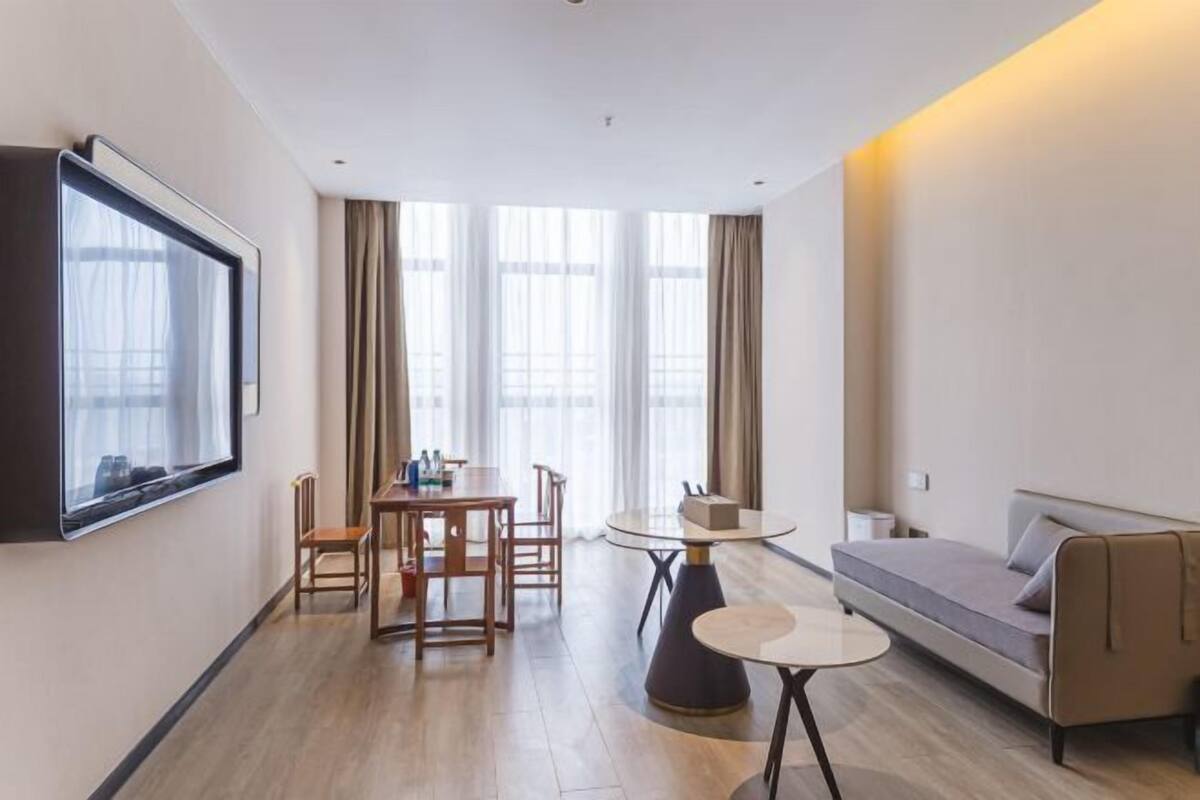 Una habitación de hotel moderna con comedor, sofá y televisor montado en la pared.