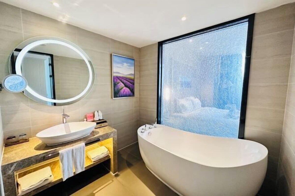 A modern bathroom with a freestanding bathtub, a round mirror, and a large window with a water feature.