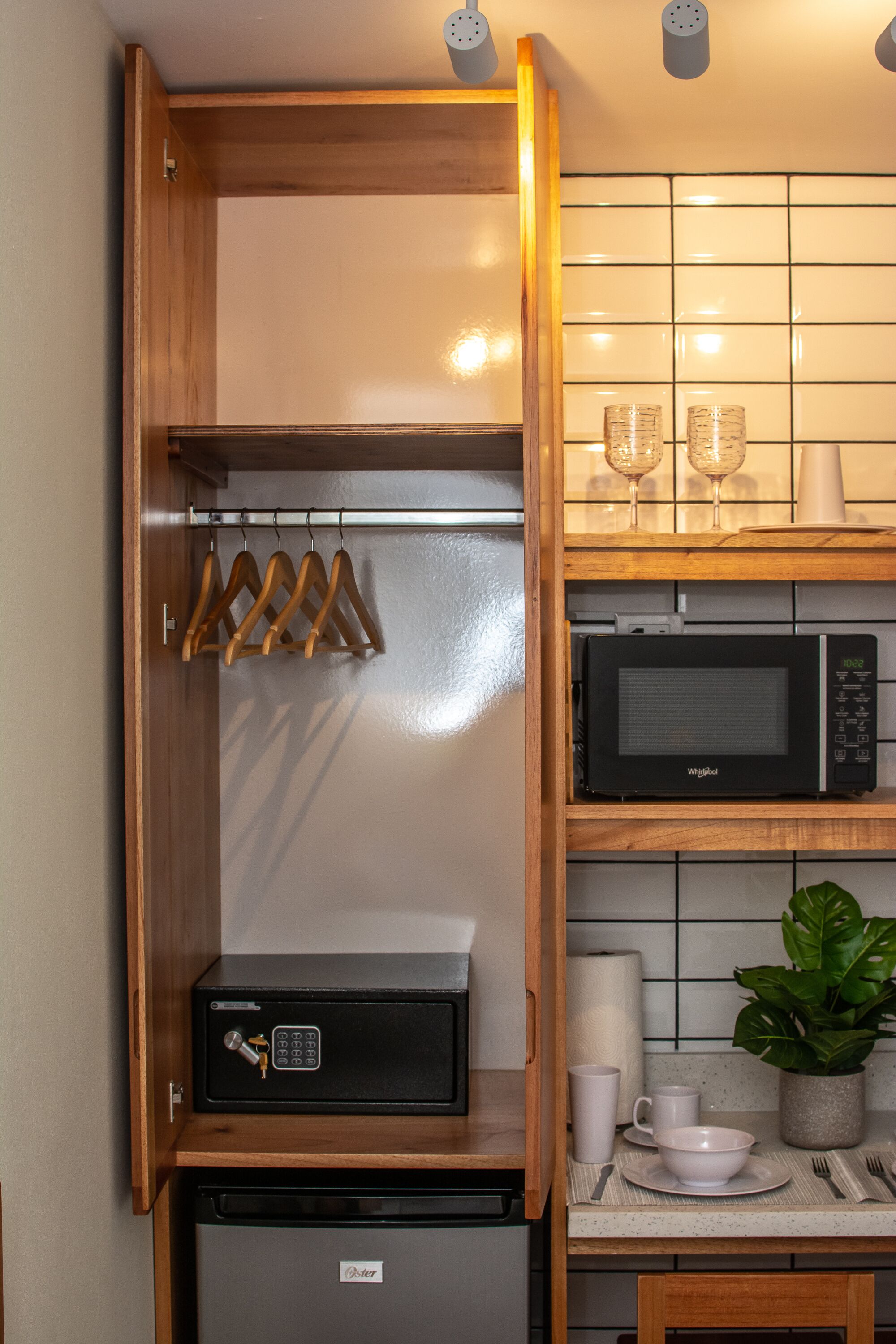 Een kleine keuken met een magnetron, een koelkastje en een houten kastje met een hangrek.