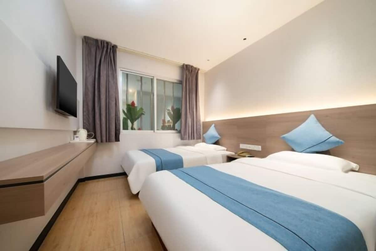 A hotel room with two beds, a TV, a window with curtains, a bedside table, and a wooden headboard.