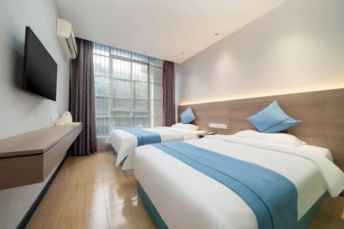 A hotel room with two beds, a flat-screen TV, a desk, and a window with curtains.
