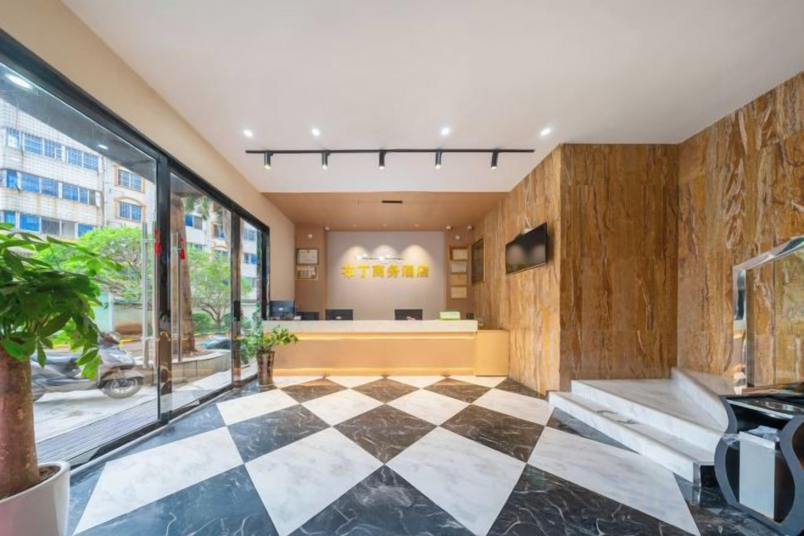 A hotel reception area with a check-in counter, a large potted plant, and a checkered floor pattern.