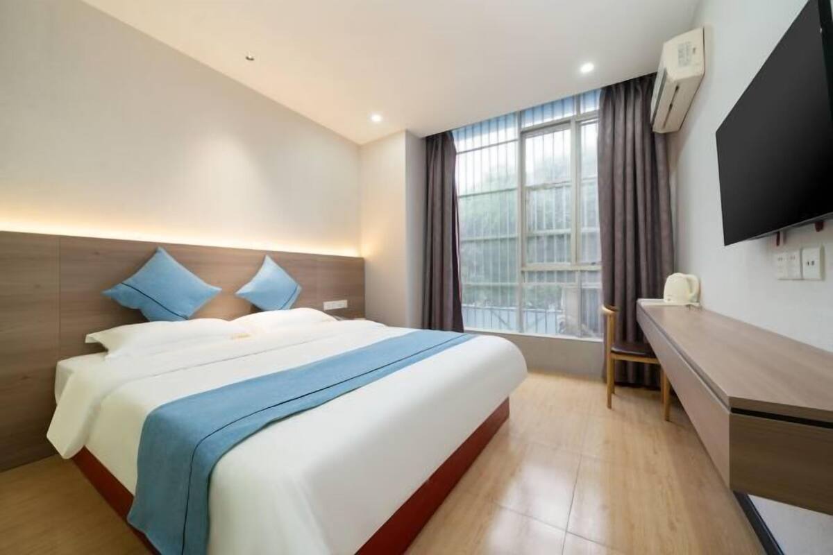 A hotel room with a large bed, a desk, a chair, a TV, and a window with curtains.