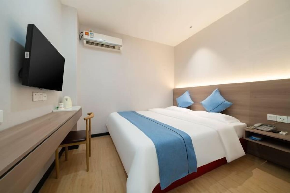 Quarto de hotel moderno com cama, mesa de cabeceira e televisão de tela plana fixada na parede.