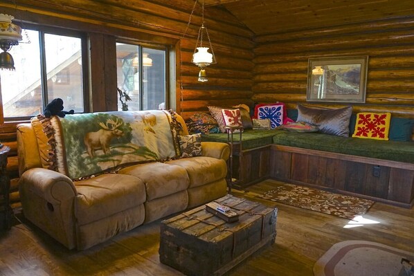 A log cabin interior with a leather sofa, a wooden coffee table, and a bench with colorful cushions.