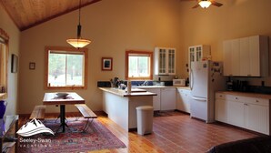 A spacious kitchen with wooden beams, a dining area with a table and benches, and a large window providing natural light.