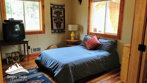 A bedroom with a bed, a television on a stand, a lamp, and a wall hanging.