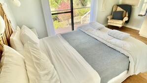 Ein Schlafzimmer mit einem großen Bett, einem Sessel, einem Balkon und Blick auf Bäume.