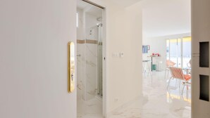 A modern interior with a glass shower, a dining area with orange chairs, and a white marble floor. - Luxurious 2-room Apartment in Palm Beach (Cannes)