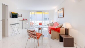A modern living room with a sofa, a chair, a small table, and a TV mounted on the wall. - Luxurious 2-room Apartment in Palm Beach (Cannes)