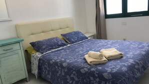 Una cama bien tendida con una colcha estampada con motivos florales, dos almohadas y dos toallas enrolladas sobre la cama.