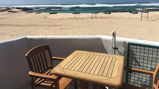 Vista de una playa desde un bote, con una mesa, sillas, un flotador salvavidas y una baranda de metal.
