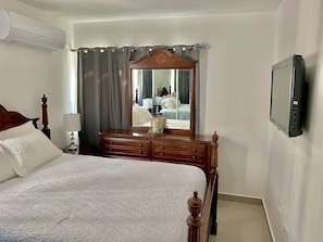 Hotellihuone, jossa on sänky, lipasto, peili, televisio ja ilmastointilaite.