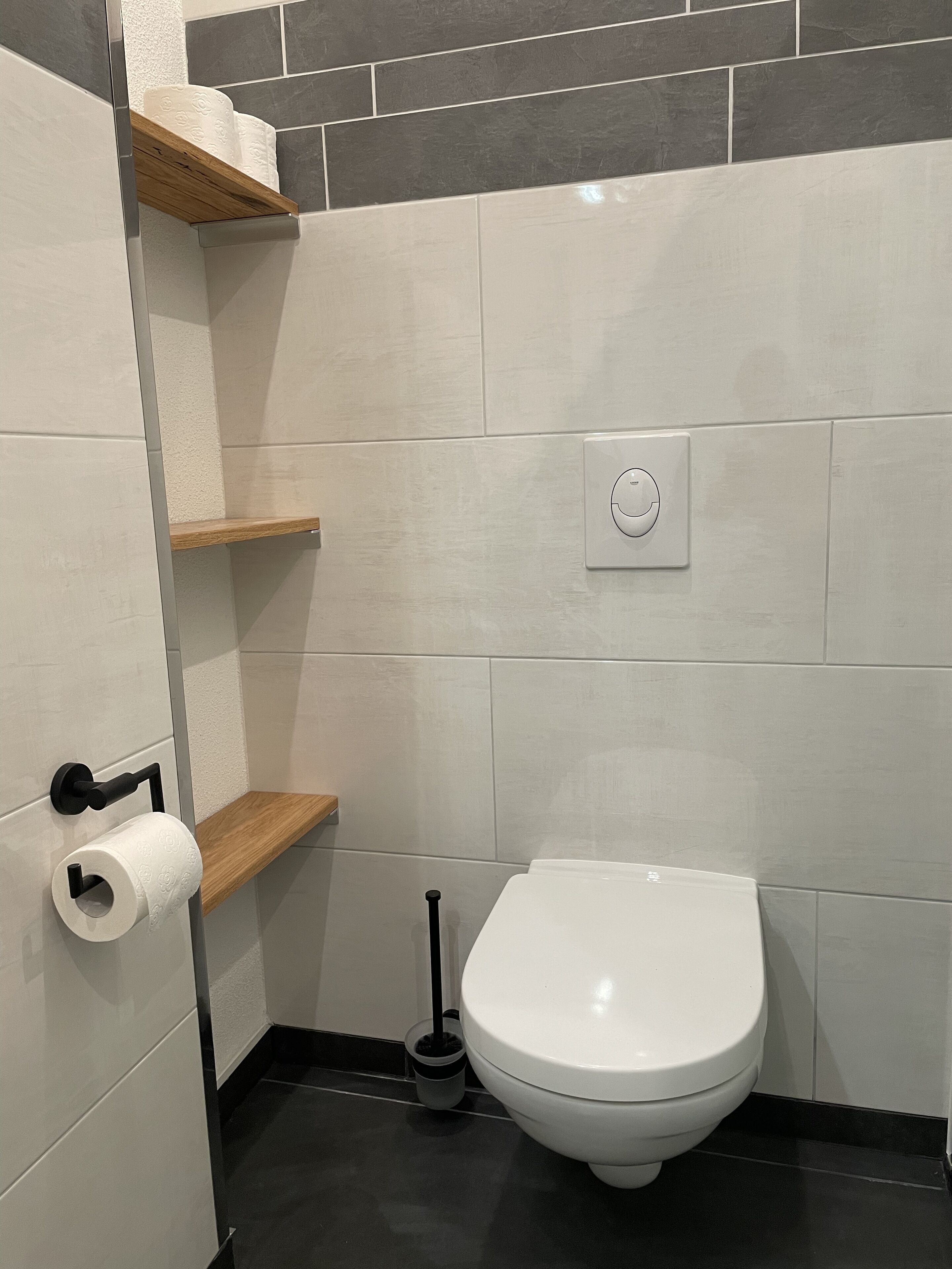 Ein Badezimmer mit Toilette, Toilettenpapier, Spülhebel und WC-Bürste.