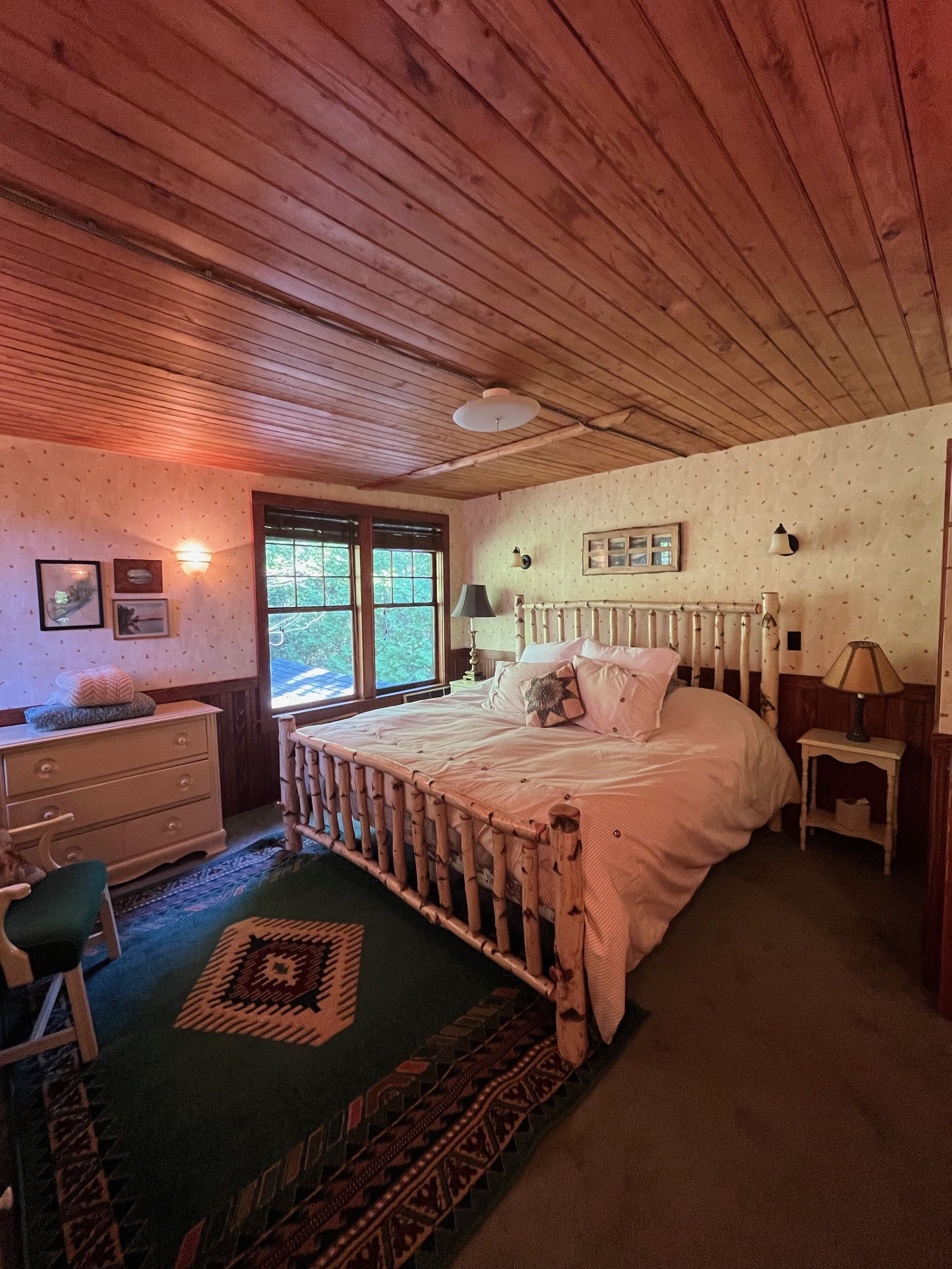 Ein Schlafzimmer mit Holzwänden, einem Bett, einem Schminktisch und einem Fenster.