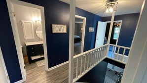 A staircase leading to a second floor with a wooden railing, a sign reading "HOWDY" on the wall, and a hallway with a dark blue wall and wooden flooring. - Gig`em on Glade-Spacious 5BR Home w/ Huge Backyard near TAMU (College Station)