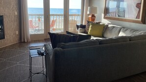 Ein Wohnzimmer mit Sofa, Fernseher, Lampe und Gemälde. Ein Balkon bietet Blick auf den Ozean.