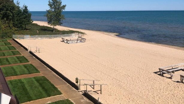 Ein Strand mit freiem Blick auf das Meer, ein Sandbereich mit Picknicktischen und ein Grasweg zum Strand.