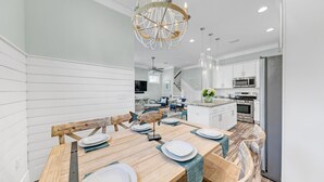 A modern kitchen with white cabinetry, stainless steel appliances, and a dining area with wooden tables and chairs.