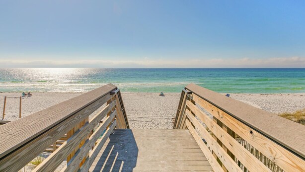 A wooden boardwalk leading to a beach with clear skies and calm waters.
