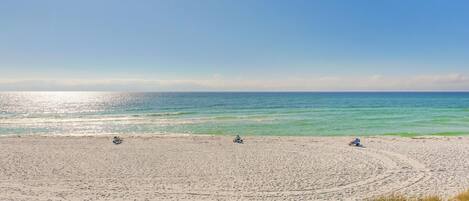 A wide sandy beach with clear blue water and a few people relaxing.
