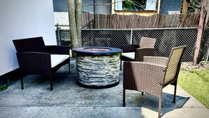 An outdoor patio area with wicker furniture, a round stone fire pit, and a chain-link fence. - City Oasis - Historic Blackrock- Pets and Parking (Buffalo)