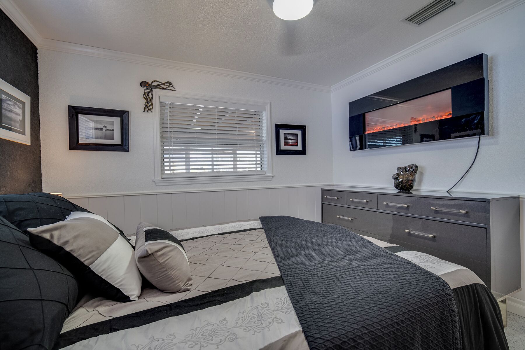 A bedroom with a bed, a dresser, a mirror, and framed pictures on the wall.