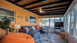 A living room with a sofa, a bean bag, a TV, and a window with blinds. - 50’ of Dock for your boats. Hot tub, Boatlift, walk 2 restaurants Xtra parking.  (Matlacha)