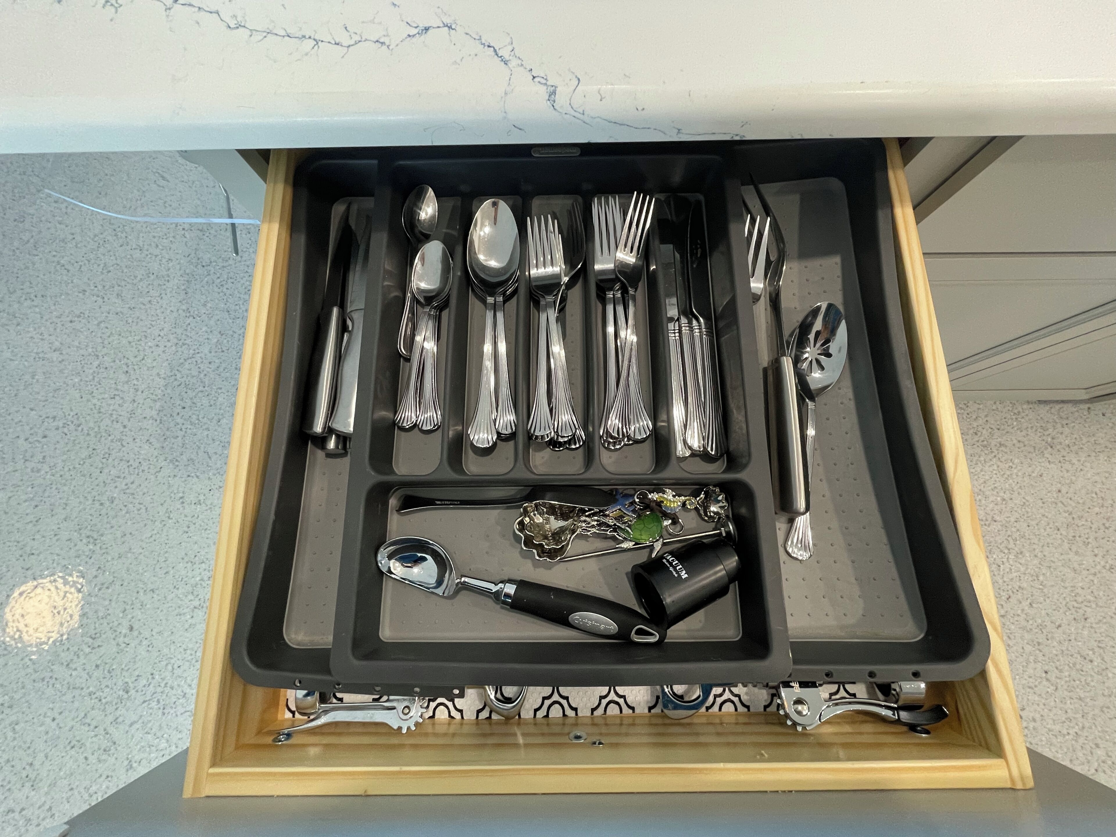 A drawer containing various kitchen utensils including spoons, forks, knives, and a can opener.