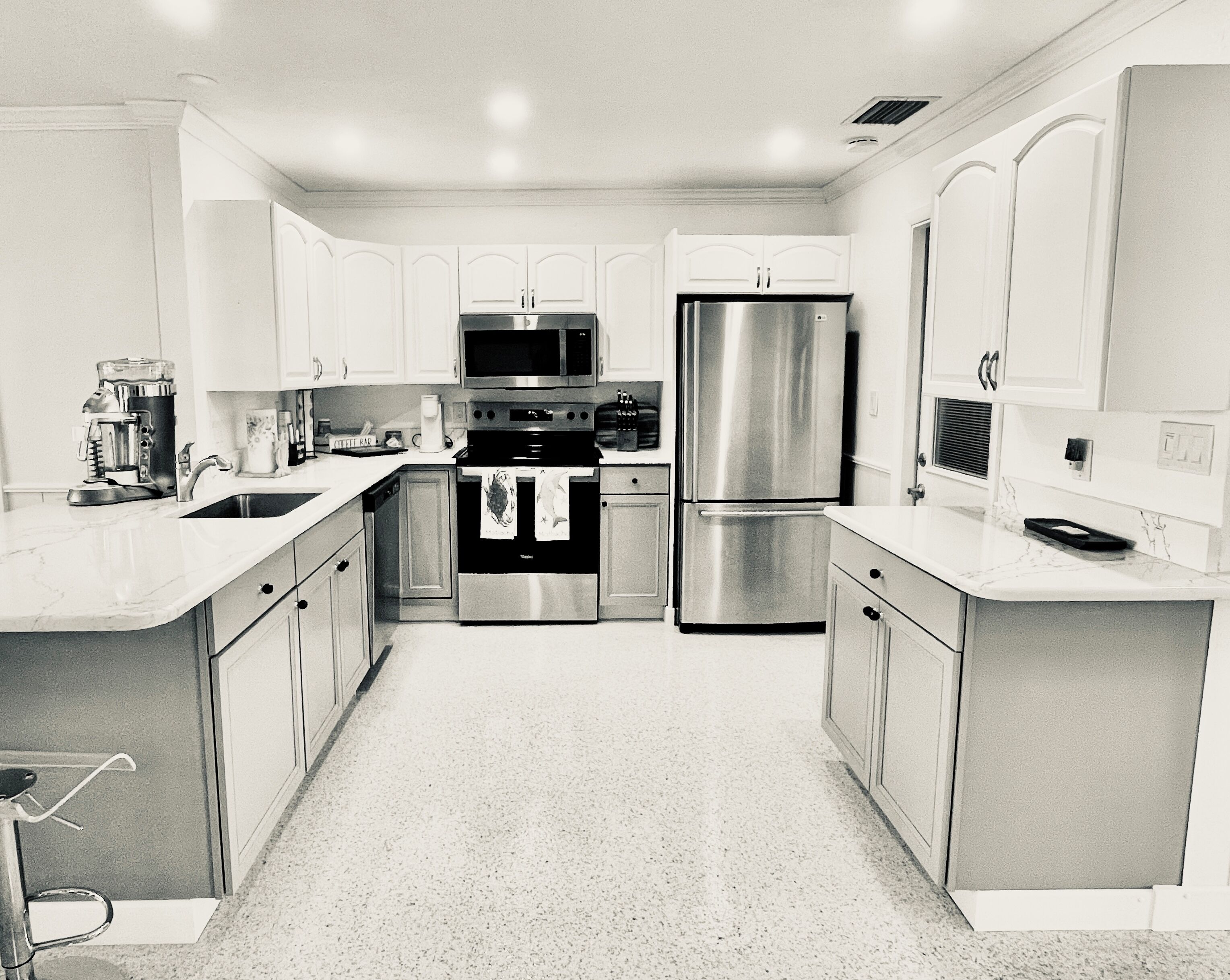 A modern kitchen with stainless steel appliances, white cabinetry, and a marble countertop.