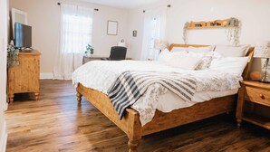 A bedroom with a wooden bed, white curtains, a ceiling fan, a wooden dresser, and a bedside table with a lamp. - Charming Palm Beach Home Close to Beaches (Tequesta)