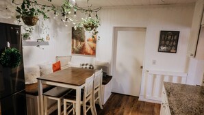 A kitchen with a wooden table, chairs, a refrigerator, hanging plants, and a painting on the wall. - Charming Palm Beach Home Close to Beaches (Tequesta)