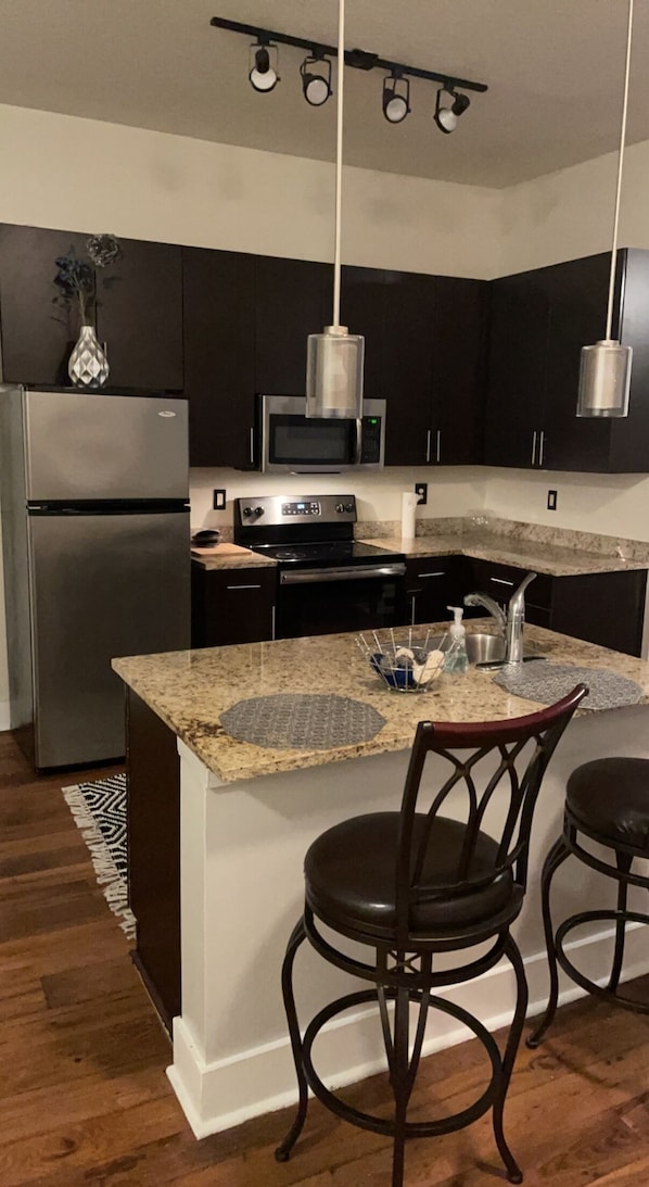 Enjoy cooking in this well-equipped kitchen with a refrigerator, microwave, and stove, as well as a granite countertop and pendant lighting.
