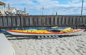 Un kayak con un design giallo e arancione, un remo e un casco su una spiaggia sabbiosa.
