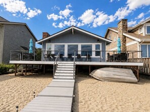 A beachfront property with a covered deck, outdoor seating, and a boat.