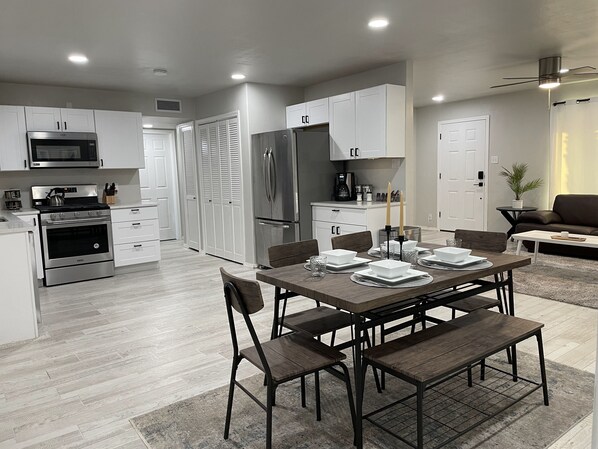 A modern kitchen with white cabinets, stainless steel appliances, and a dining area with a wooden table and chairs.
