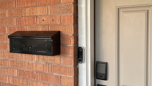 Pared de ladrillo con buzón y puerta con cerradura electrónica.