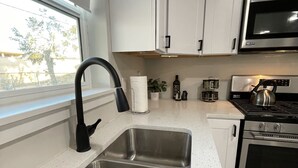 Una cocina moderna con un lavaplatos de acero inoxidable, armarios blancos, un microondas y una estufa.