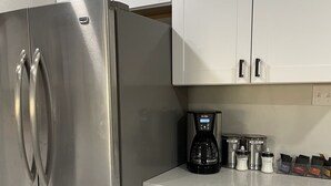Una cocina con un refrigerador de acero inoxidable, gabinetes blancos y una cafetera sobre la encimera.