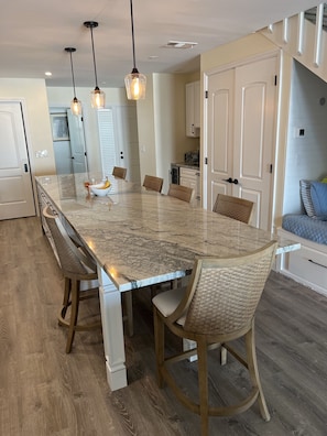 A spacious kitchen with a large island, wooden chairs, pendant lighting, and a view of the living area.