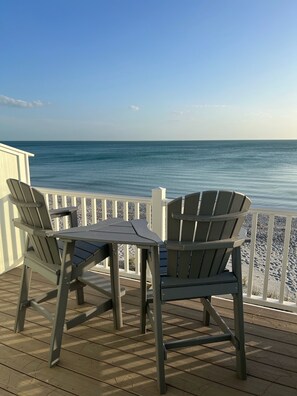 Eine Terrasse mit zwei Adirondack-Stühlen und einem Tisch, mit Blick auf ein ruhiges Meer.