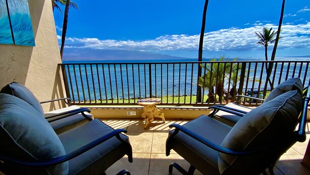 A balcony with two lounge chairs, a small table, and a view of the ocean and mountains. - LUANA MOANA SIGNATURE OCEANFRONT MAUI-Ocean&Haleakala Views-FreeWiFi-A/C-Romance (Wailuku)