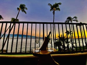 En balkon med udsigt over havet og palmer, en flaske og et glas.