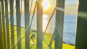 A person on a yoga mat practicing yoga on a grassy area near a body of water, with a sunset in the background. - LUANA MOANA SIGNATURE OCEANFRONT MAUI-Ocean&Haleakala Views-FreeWiFi-A/C-Romance (Wailuku)