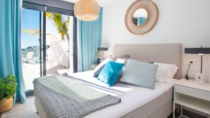 Un dormitorio con cama, mesita de noche, lámpara, espejo y vistas al exterior.